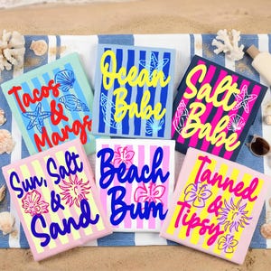 Puede incluir: Una colecci&oacute;n de dise&ntilde;os cuadrados y coloridos con tem&aacute;tica playera, con texto e ilustraciones. Los dise&ntilde;os incluyen frases como "Tacos & Marg", "Ocean Babe", "Salt Babe", "Sun, Salt & Sand", "Beach Bum" y "Tanned & Tipsy". Sobre una toalla de playa.