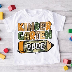 May include: White t-shirt with a colorful graphic of a pencil with the words "Kindergarten Dude" on it.