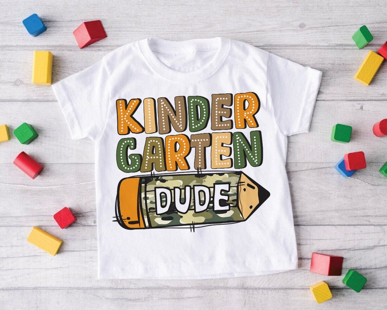 May include: White t-shirt with a colorful graphic of a pencil with the words "Kindergarten Dude" on it.