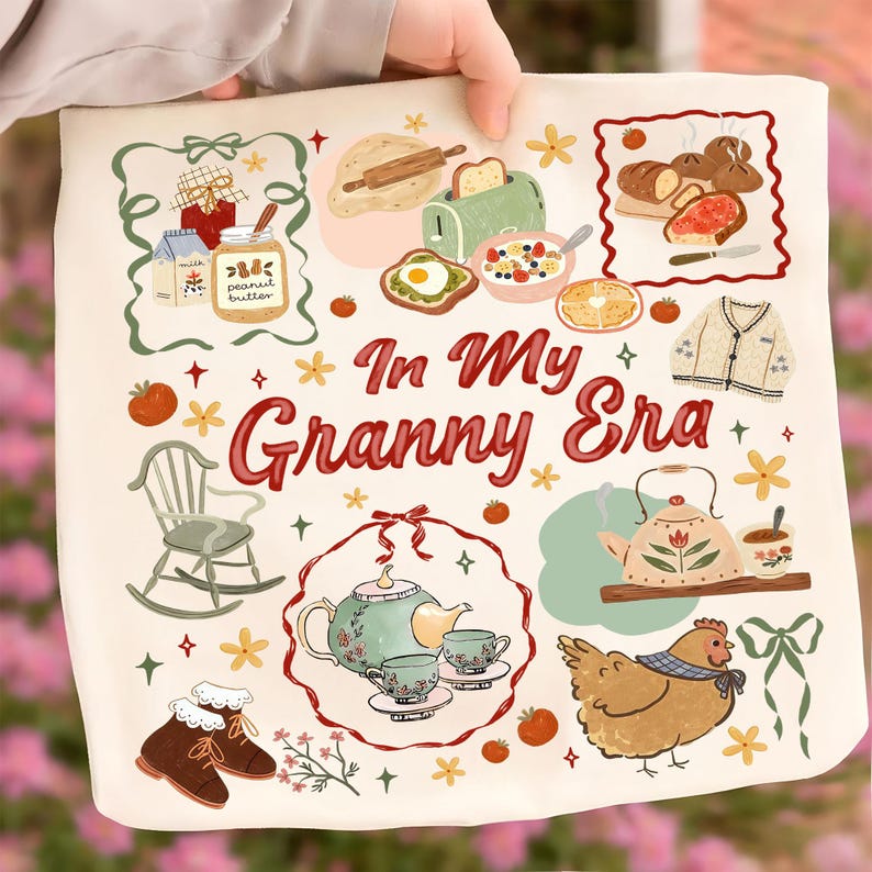 以下が含まれることがあります： クリーム色のトートバッグ。赤い筆記体で「In My Granny Era」の文字。ロッキングチェア、ティーポット、トースト、鶏のイラストが特徴で、居心地の良いヴィンテージ感を醸し出しています。デザインには花柄や食べ物関連の要素が含まれています。