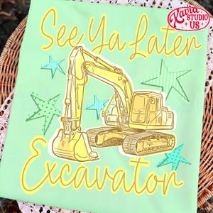 Pu&ograve; includere: Maglietta verde chiaro con un'illustrazione di escavatore giallo e la scritta "See Ya Later Excavator". Il design include stelle gialle e blu e un logo nell'angolo in alto a destra.