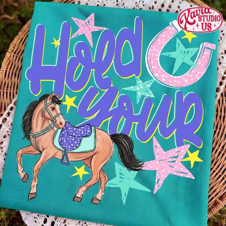 May include: Teal t-shirt with a horse illustration and the text "Hold Your Horses" in purple and white. The horse has a saddle and is surrounded by stars in pink, teal, and yellow. A horseshoe graphic is also present.
