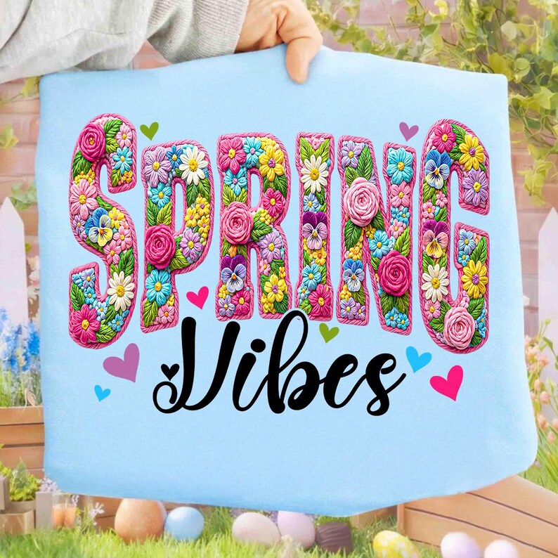 Puede incluir: Tela azul claro con las palabras "SPRING VIBES" en un dise&ntilde;o floral. Las letras est&aacute;n llenas de flores coloridas, incluyendo rosas, margaritas y pensamientos. Peque&ntilde;os corazones en rosa, verde y azul rodean el texto.