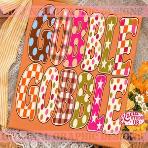 May include: A rectangular orange sign featuring the text GOBBLE GOBBLE in large, colorful, patterned letters. The letters display various designs including polka dots, plaid, checkered patterns, and stars in shades of pink, orange, green, and brown.