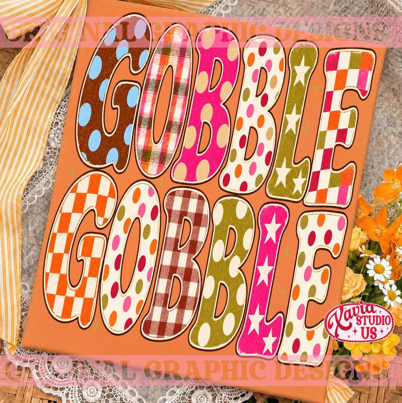 May include: A rectangular orange sign featuring the text GOBBLE GOBBLE in large, colorful, patterned letters. The letters display various designs including polka dots, plaid, checkered patterns, and stars in shades of pink, orange, green, and brown.