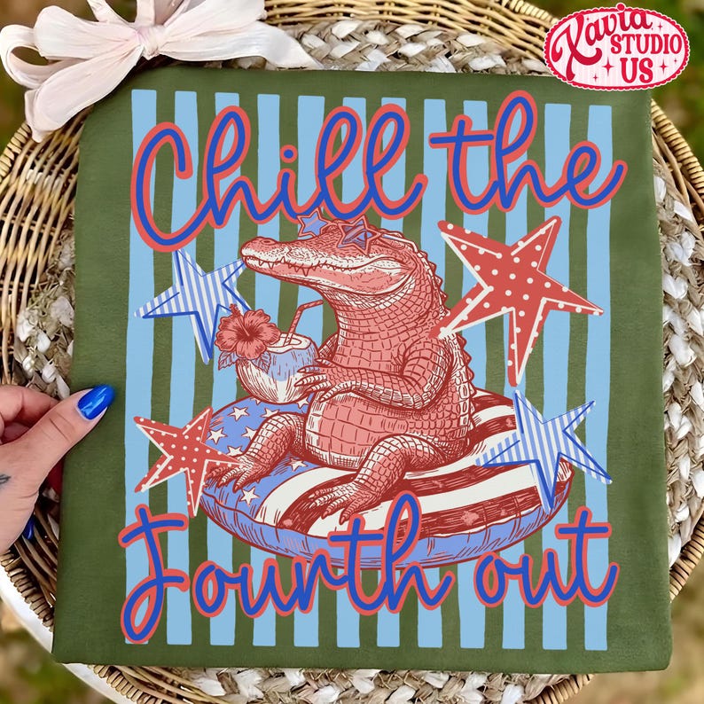 May include: Olive green t-shirt with a Fourth of July theme. The design features an alligator wearing sunglasses and floating on an inner tube, holding a tropical drink. The text "Chill the Fourth out" is written in red and blue.