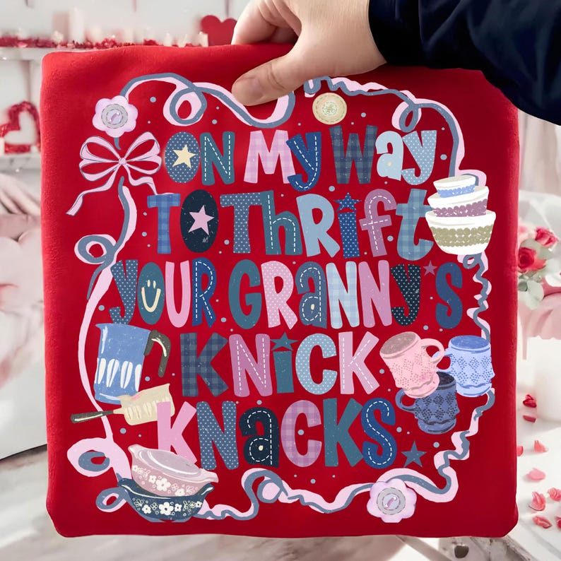 Peut inclure: Coussin rouge avec l'inscription "ON MY WAY TO THRIFT YOUR GRANNY'S KNICK KNACKS" dans une typographie color&eacute;e et fantaisiste. Le motif comprend des illustrations de tasses, de bols et d'une th&eacute;i&egrave;re, le tout encadr&eacute; par une bordure d&eacute;corative.