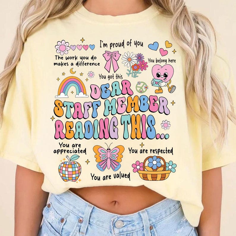 May include: A yellow t-shirt with a colorful graphic that says "Dear Staff Member Reading This..." with illustrations of hearts, flowers, butterflies, and rainbows. The text says "You are appreciated, You are respected, You are valued".