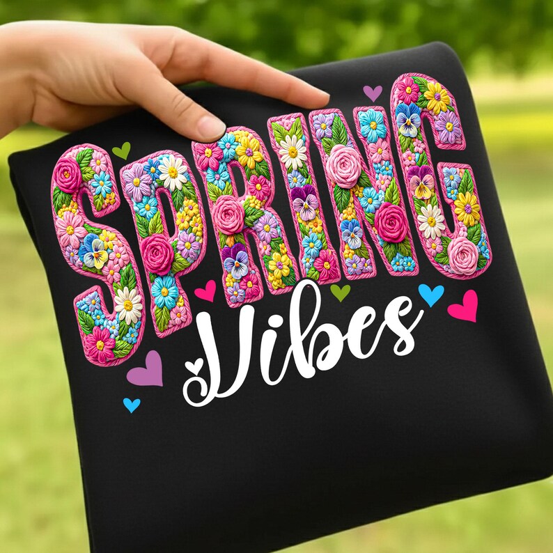 Puede incluir: Camiseta negra con la frase "SPRING Vibes". La palabra "SPRING" est&aacute; adornada con un dise&ntilde;o floral colorido, mientras que "Vibes" est&aacute; escrita en blanco. El dise&ntilde;o incluye peque&ntilde;os corazones de varios colores.