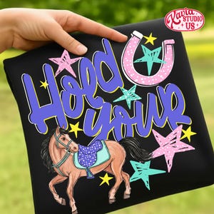 May include: Black t-shirt with a horse illustration and the text "Hold Your". The horse is brown with a blue saddle. Pink, blue, and yellow stars and a pink horseshoe decorate the shirt.