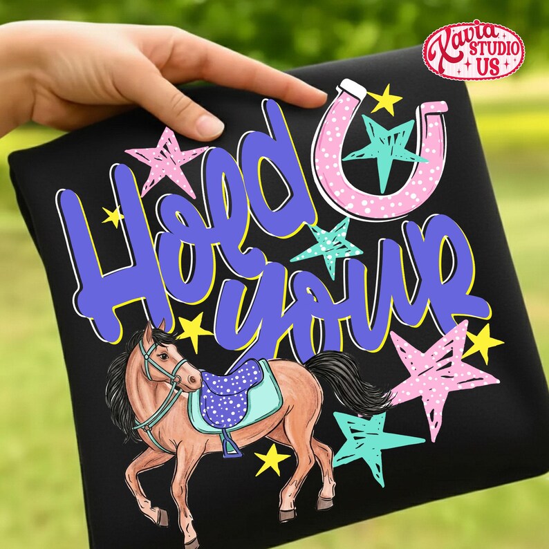May include: Black t-shirt with a horse illustration and the text "Hold Your". The horse is brown with a blue saddle. Pink, blue, and yellow stars and a pink horseshoe decorate the shirt.