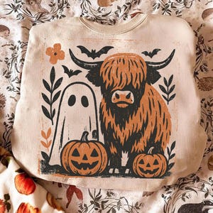 Può includere: Felpa beige con grafica a tema Halloween. Il design include una mucca delle Highlands, un fantasma, due zucche intagliate, pipistrelli ed elementi floreali neri e arancioni. Girocollo, maniche lunghe.