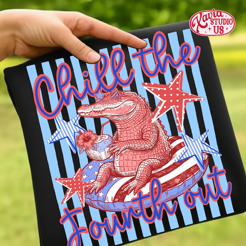 May include: Black t-shirt with a Fourth of July design. The graphic features a red alligator wearing sunglasses and floating on an inner tube. The text reads "Chill the Fourth out" in blue and red.