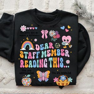 May include: Black sweatshirt with a rainbow, flowers, and a heart design. The text reads "Dear Staff Member Reading This... You are appreciated. You are respected. You are valued."