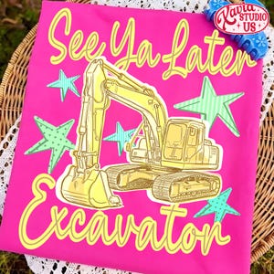 Pu&ograve; includere: Una maglietta rosa acceso con la scritta "See Ya Later Excavation" in giallo. Una grafica di escavatore giallo &egrave; centrata, circondata da stelle verdi e blu. La maglietta ha un bordo in pizzo bianco.