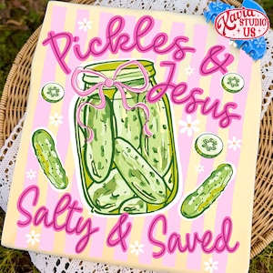 May include: A decorative sign with the words "Pickles & Jesus Salty & Saved" in pink script. The design features a jar of pickles with a pink bow, cucumber slices, and white flowers on a yellow and pink striped background.