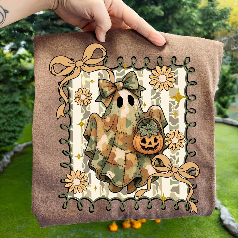 May include: A brown square pillow featuring a Halloween ghost design. The ghost wears a camouflage outfit and holds a jack-o'-lantern basket. The design includes bows, daisies, and a decorative border. The background is a striped pattern.