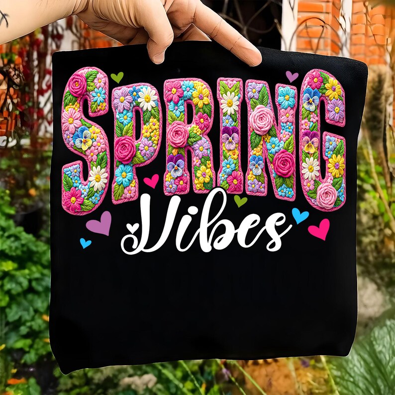 Puede incluir: Bolso tote negro con las palabras "SPRING Vibes". La palabra "SPRING" est&aacute; escrita en letras grandes y florales, con una variedad de flores. "Vibes" est&aacute; en una fuente cursiva, con corazones alrededor del texto. Un dise&ntilde;o alegre con tem&aacute;tica primaveral.