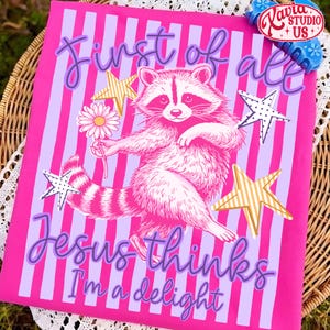 May include: A pink graphic tee with a raccoon illustration holding a daisy, surrounded by stars. The text reads "First of all Jesus thinks I'm a delight" in purple script. The background has vertical stripes.