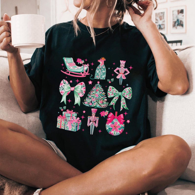 May include: Black t-shirt featuring a festive Christmas design. The design includes a sleigh, bows, a Christmas tree, presents, and a nutcracker, all in shades of pink, green, and white.