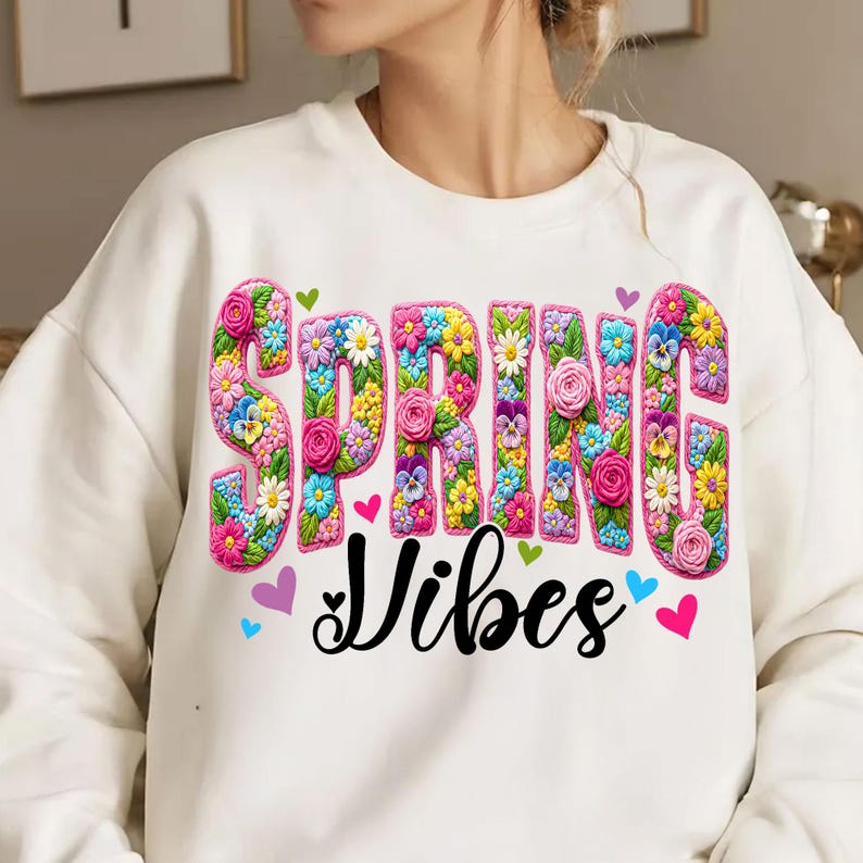 Puede incluir: Sudadera blanca con la frase "SPRING Vibes". La palabra "SPRING" est&aacute; en un dise&ntilde;o floral colorido en 3D. El dise&ntilde;o incluye rosas, margaritas y pensamientos. Peque&ntilde;os corazones multicolores.