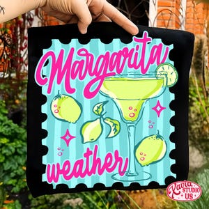 May include: Black square cushion with a colourful design. The design features a margarita cocktail, lemons, and the words "Margarita weather" in pink and teal. The cushion has a stamp-like border.