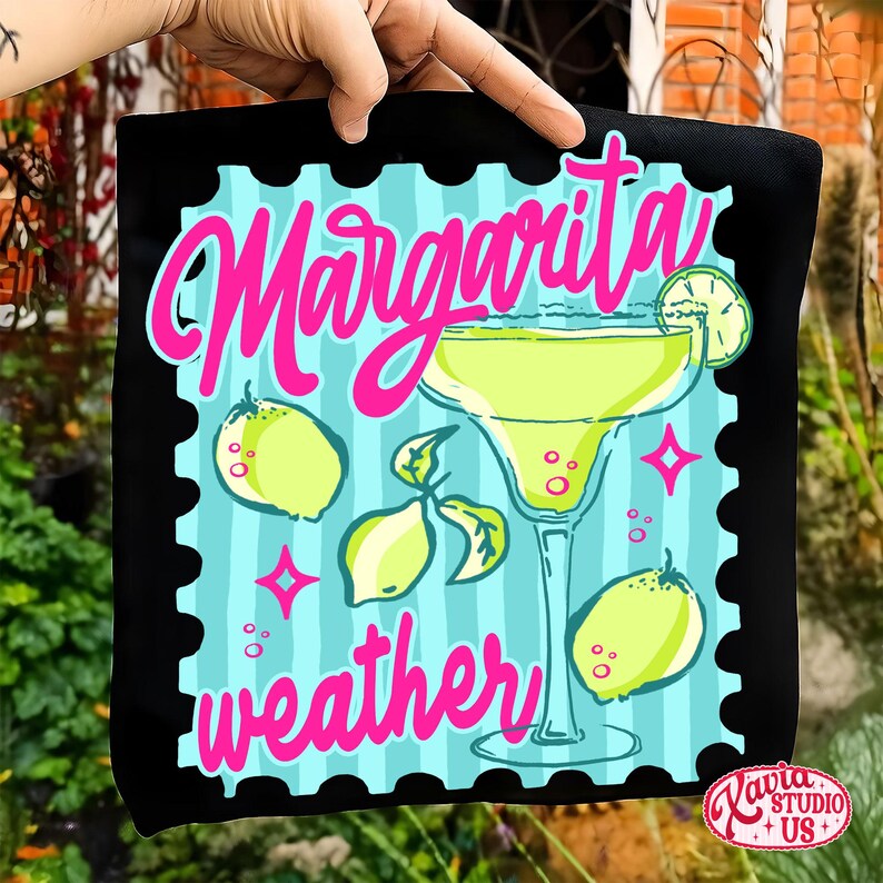 May include: Black square cushion with a colourful design. The design features a margarita cocktail, lemons, and the words "Margarita weather" in pink and teal. The cushion has a stamp-like border.