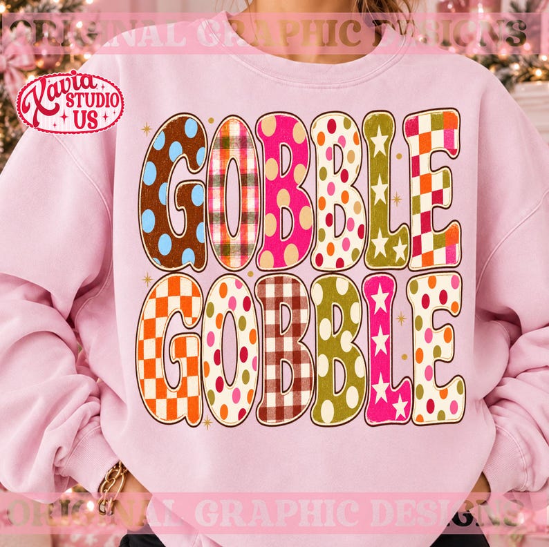 May include: A light pink crewneck sweatshirt featuring the text GOBBLE GOBBLE in large, bold letters. Each letter is filled with a different pattern, including polka dots, plaid, checkered prints, and stars in shades of brown, orange, pink, and green.