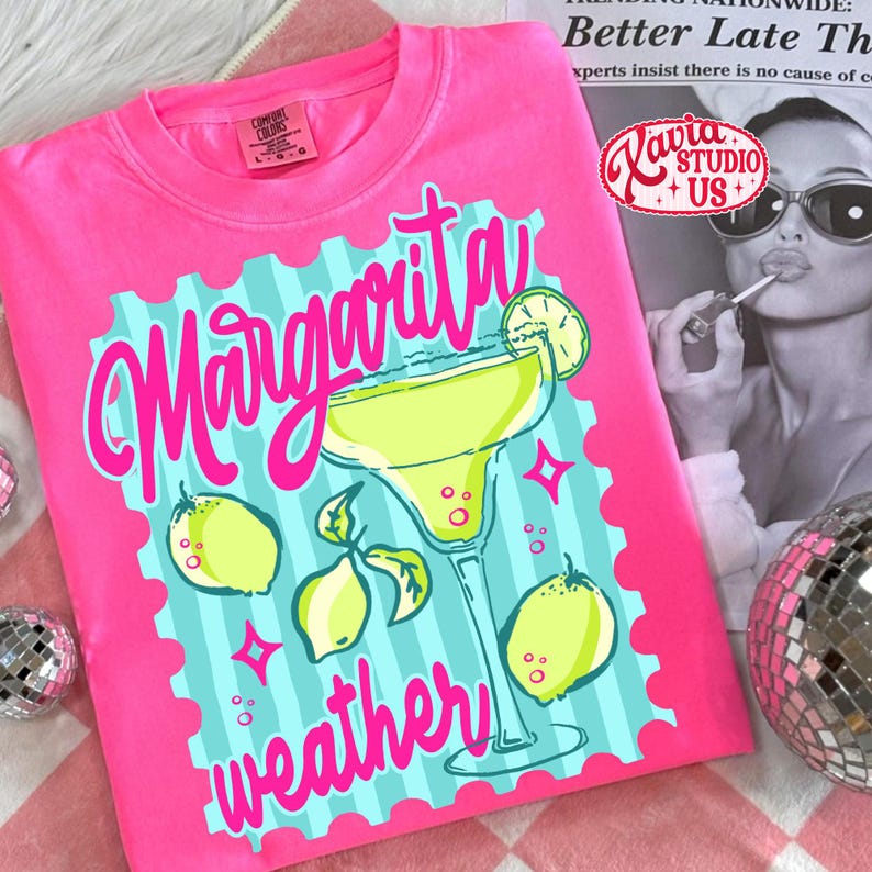 May include: A vibrant pink t-shirt with the words "Margarita weather" in a fun font. The design includes a margarita glass, lemons, and a turquoise and pink border. The shirt is a Comfort Colors brand.