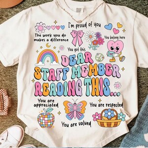 May include: A white t-shirt with a colorful graphic design that says "Dear Staff Member Reading This..." with a rainbow, butterfly, apple, and other cute illustrations. The text also says "I'm proud of you", "You got this", "You are appreciated", "You are respected", and "You are valued".