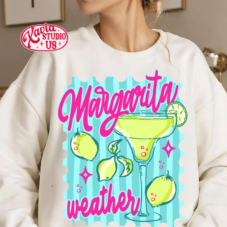 May include: Cream-coloured sweatshirt with a vibrant graphic. The design includes a margarita cocktail, lemons, and the words "Margarita weather" in pink script. The design is set against a blue background.