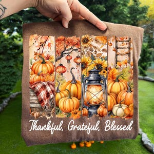 May include: Brown fabric with a fall-themed graphic featuring pumpkins, sunflowers, and a lantern. The text "Thankful, Grateful, Blessed" is written in white script across the bottom. The image evokes a sense of autumn and harvest.