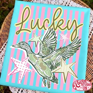 May include: A canvas print with a duck illustration and the word "Lucky" in a script font. The background is light blue with pink and white vertical stripes. The duck is green and white with star accents.