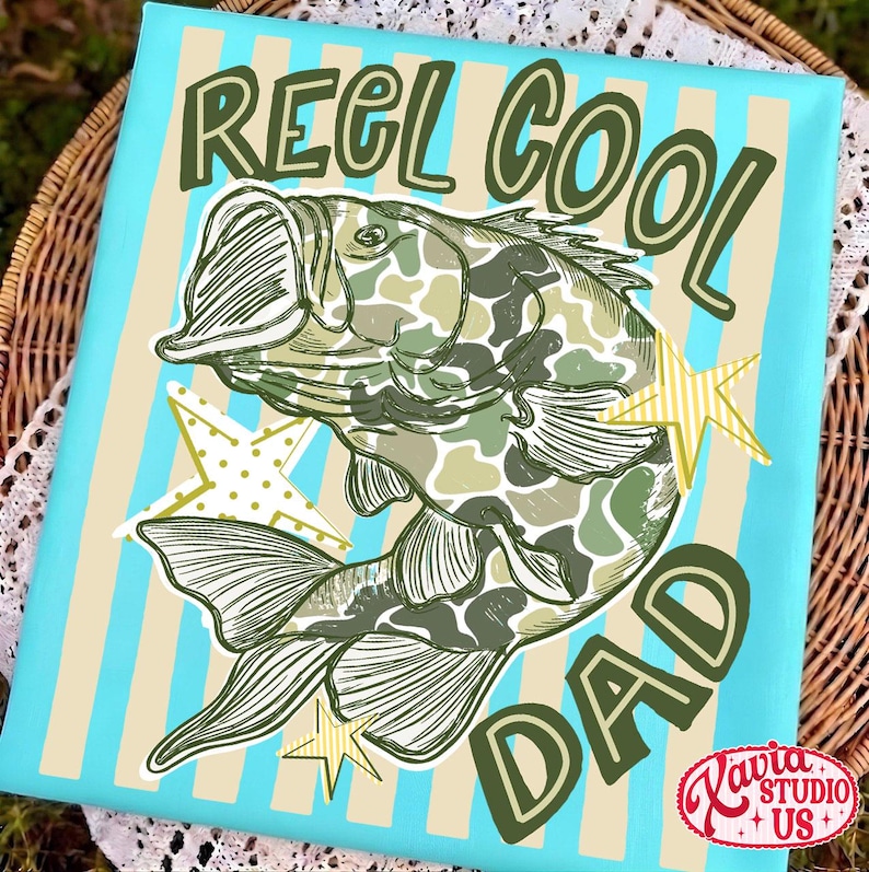 May include: Canvas art with a blue background and vertical beige stripes. The artwork features a fish with a camouflage pattern and the words "REEL COOL DAD" in green. Yellow star accents are also included.