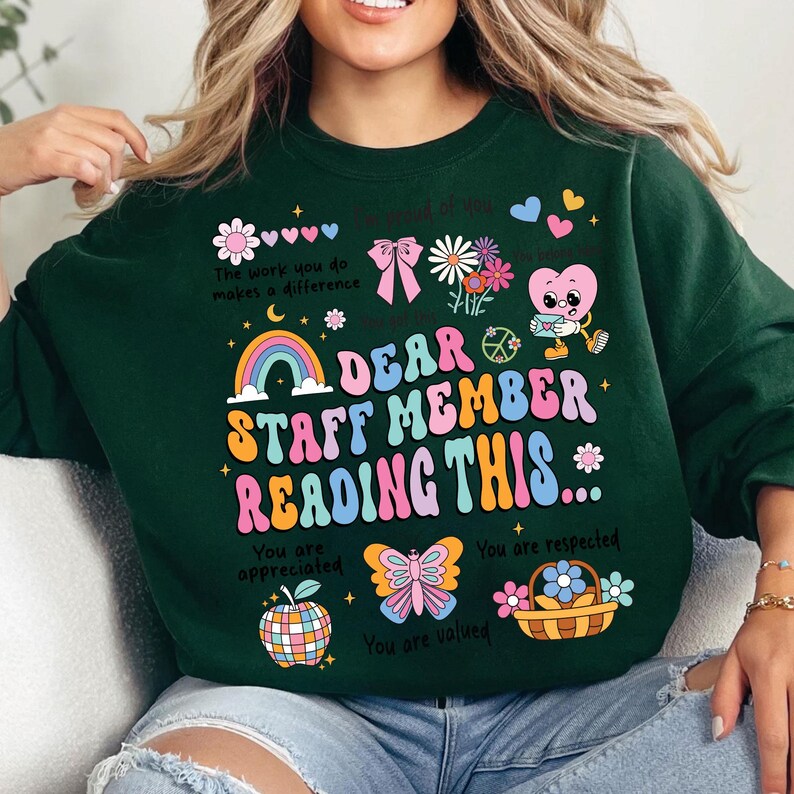 May include: Green sweatshirt with a colorful graphic design that says "Dear Staff Member Reading This..." with a rainbow, butterfly, apple, and other illustrations. The text also says "You are appreciated", "You are respected", and "You are valued".