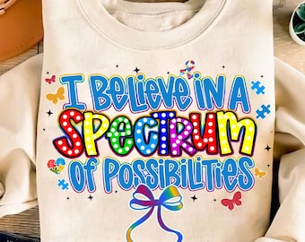 May include: Cream-colored sweatshirt with the text "I Believe in a Spectrum of Possibilities" in colorful bubble letters. The design includes puzzle pieces, butterflies, and a rainbow ribbon.
