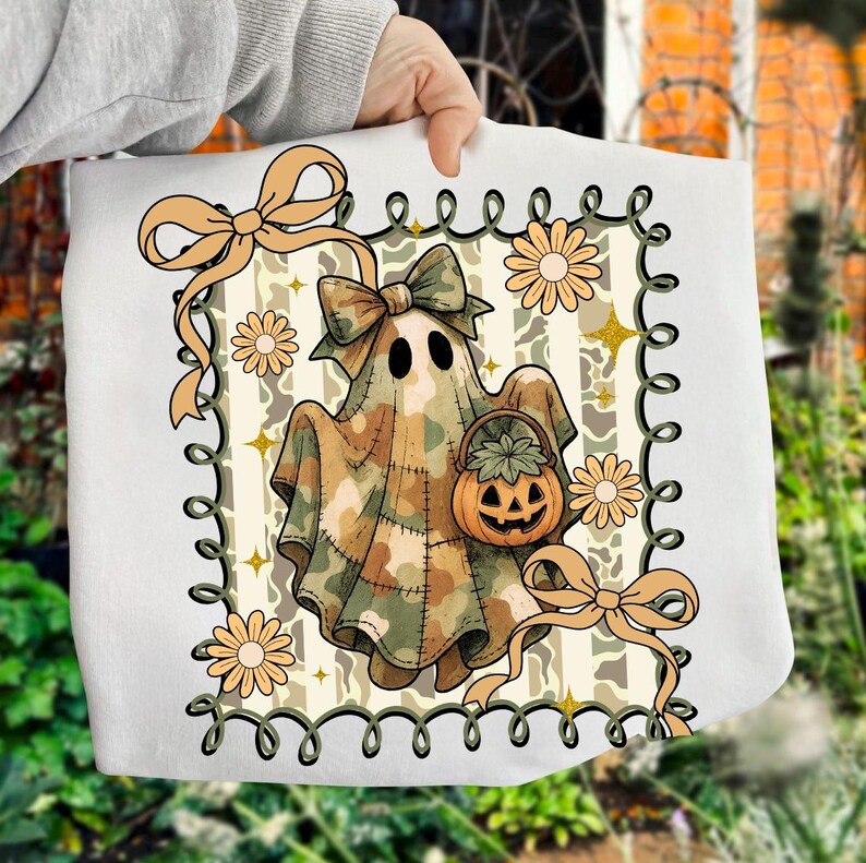 May include: White tote bag featuring a cartoon ghost in a camouflage pattern, holding a pumpkin basket. The design includes bows, flowers, and a decorative border, perfect for Halloween. The overall color scheme is beige, brown, and green.