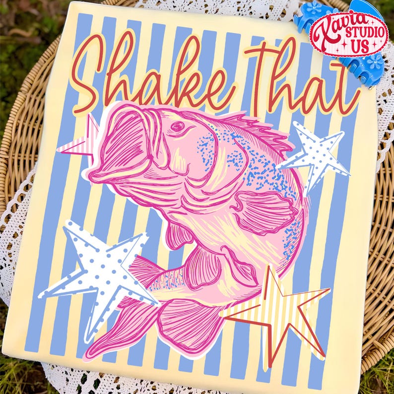May include: A decorative square featuring a pink fish illustration with the text "Shake That" in a playful font. The design includes blue and yellow stripes and star accents, creating a whimsical aesthetic.