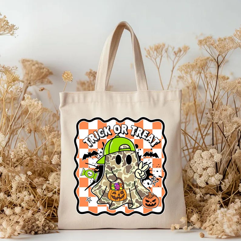 May include: A beige canvas tote bag featuring a Halloween-themed graphic. The graphic includes a cartoon ghost wearing a green cap, holding a pumpkin, and giving a peace sign. The words "TRICK OR TREAT" are displayed above the ghost on a checkered orange and white background.