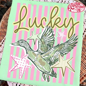 May include: A light green fabric with pink vertical stripes and the word "Lucky" in a cursive font. A duck illustration with outstretched wings is surrounded by star shapes. The image includes the text "Lavia Studio + US".