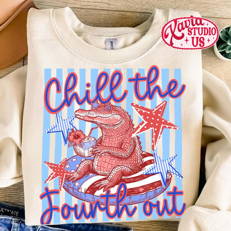 May include: Cream-colored sweatshirt with a graphic of an alligator wearing sunglasses and floating on an inner tube. The design includes red, white, and blue stars and stripes, with the text "Chill the Fourth out."