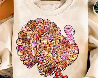 May include: A cream-colored sweatshirt featuring a colorful turkey design. The turkey has a mosaic-like pattern in shades of orange, pink, and purple. The turkey's head and feet are red. The design is centered on the front of the sweatshirt.