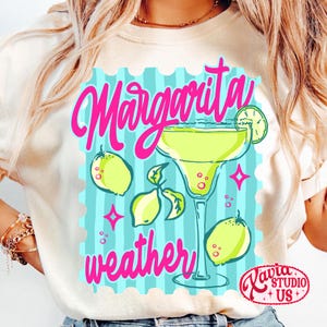 May include: A cream-coloured t-shirt with a bright graphic. It shows a margarita cocktail, lemons, and the words "Margarita weather" in pink. The design is set against a light blue background with a postage stamp border.