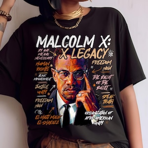 May include: Black t-shirt featuring a portrait of Malcolm X with the text "Malcolm X: X Legacy." Additional text includes "By Any Means Necessary," "Human Rights," and "Freedom Now." The design incorporates orange and white text.