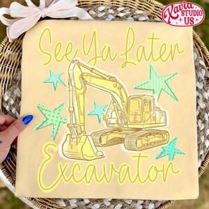 Pu&ograve; includere: Maglietta beige chiaro con un'illustrazione di escavatore giallo e la scritta "See Ya Later Excavator". Il design include stelle verdi e blu chiare, creando un look giocoso. La maglietta &egrave; probabilmente per bambini.