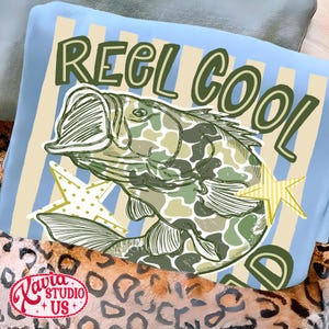 May include: A light blue pillow with the words "REEL COOL" in green lettering. A fish with a camouflage pattern is in the center, with two yellow star accents. The pillow is on a leopard print blanket.
