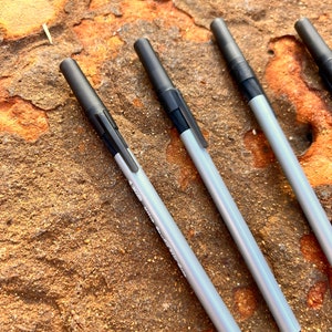 May include: Four silver pens with black tops lying on a brown, textured surface.