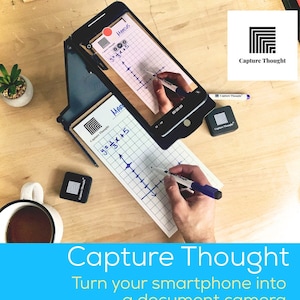 May include: A black smartphone stand with a white gridded notepad and a blue pen. The smartphone is displaying a graph with the equation "y=3x+5" and the text "Capture Thought". The stand is designed to turn a smartphone into a document camera.