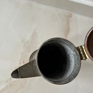 May include: A copper teapot with a hinged lid. The teapot is empty and the inside is visible.