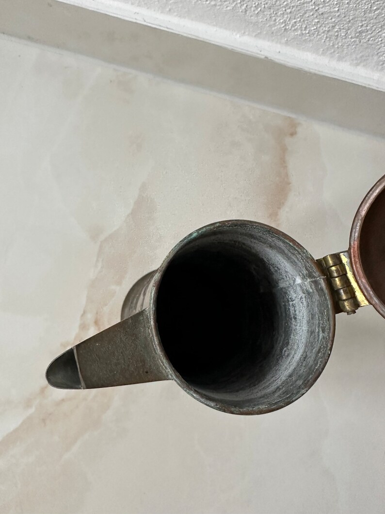 May include: A copper teapot with a hinged lid. The teapot is empty and the inside is visible.